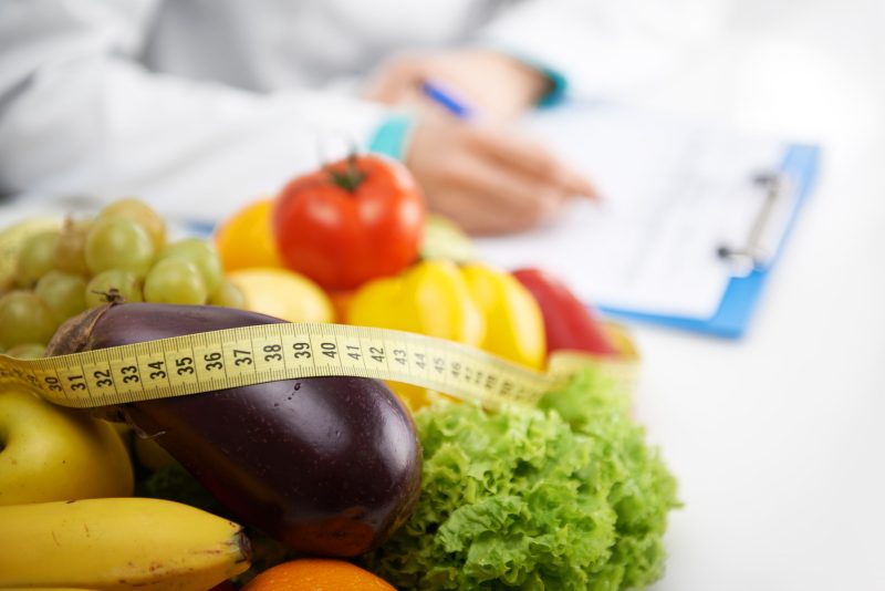 48595947 - healthy nutrition concept. close-up of fresh vegetables and fruits with measuring tape lying on doctor's desk.